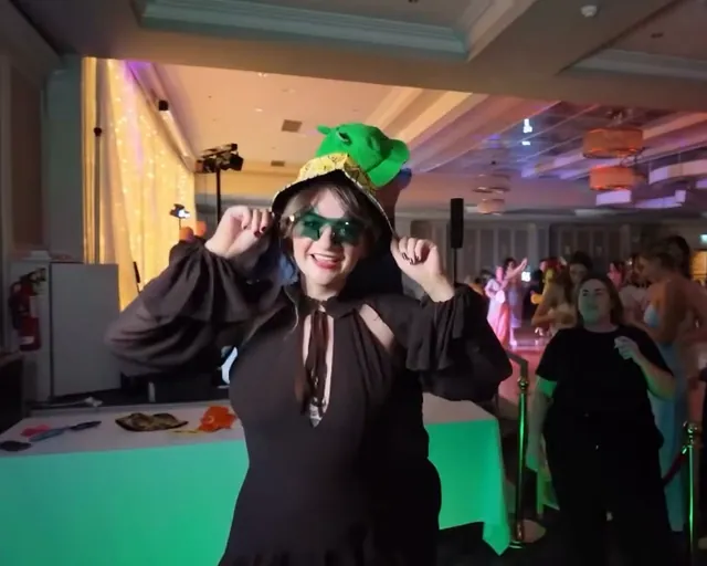 Guest in a bucket hat and sunglasses dancing, with the party behind