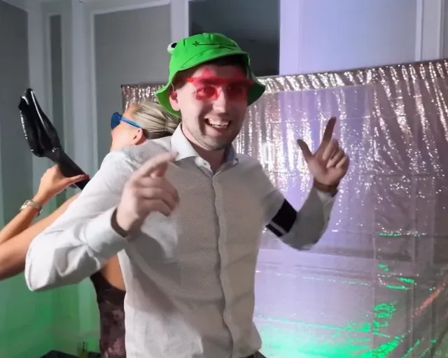 Guest in a green bucket hat and red glasses pointing at the camera